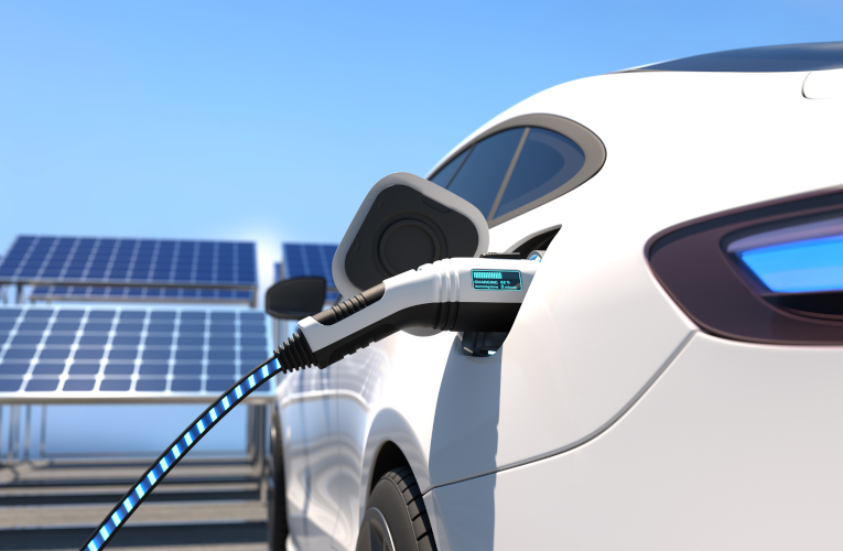 A white electric vehicle charging with solar panels in the background.